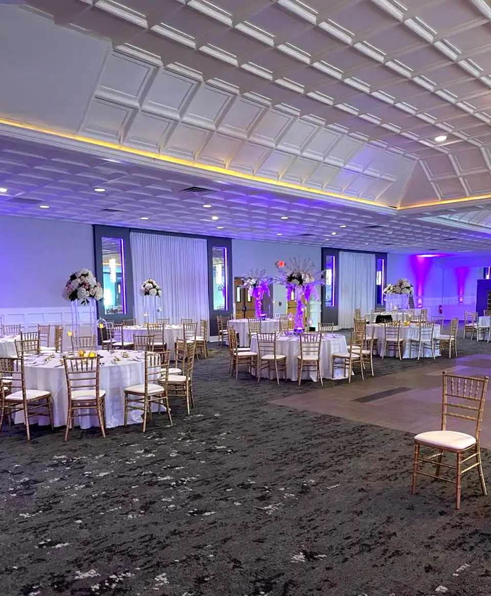 Elegant banquet hall with white table linens, gold chiavari chairs, floral centerpieces, and purple uplighting at the Macedonian Culture Center in Crown Point, Indiana
